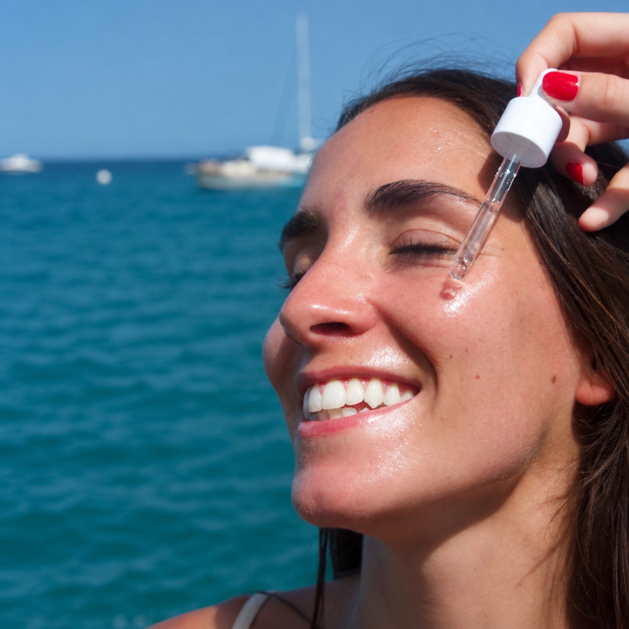 Modelo sonriendo mientras se aplica el Serum de Ácido Hialurónico Nebai Cosmetics en un barco